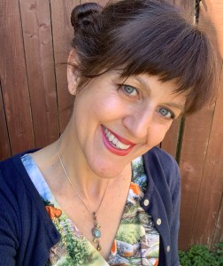Author photo: A smiling head shot of a woman with her hair in space buns wearing a fox dress and a blue cardigan sweater.